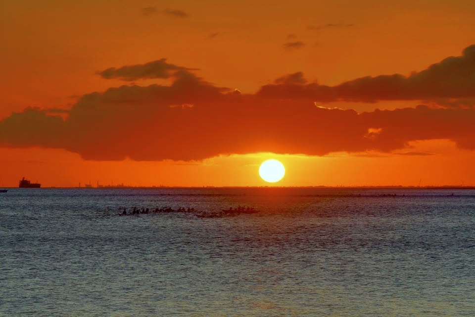 Outrigger canoes silhouetted on the water beneath an orange sunset